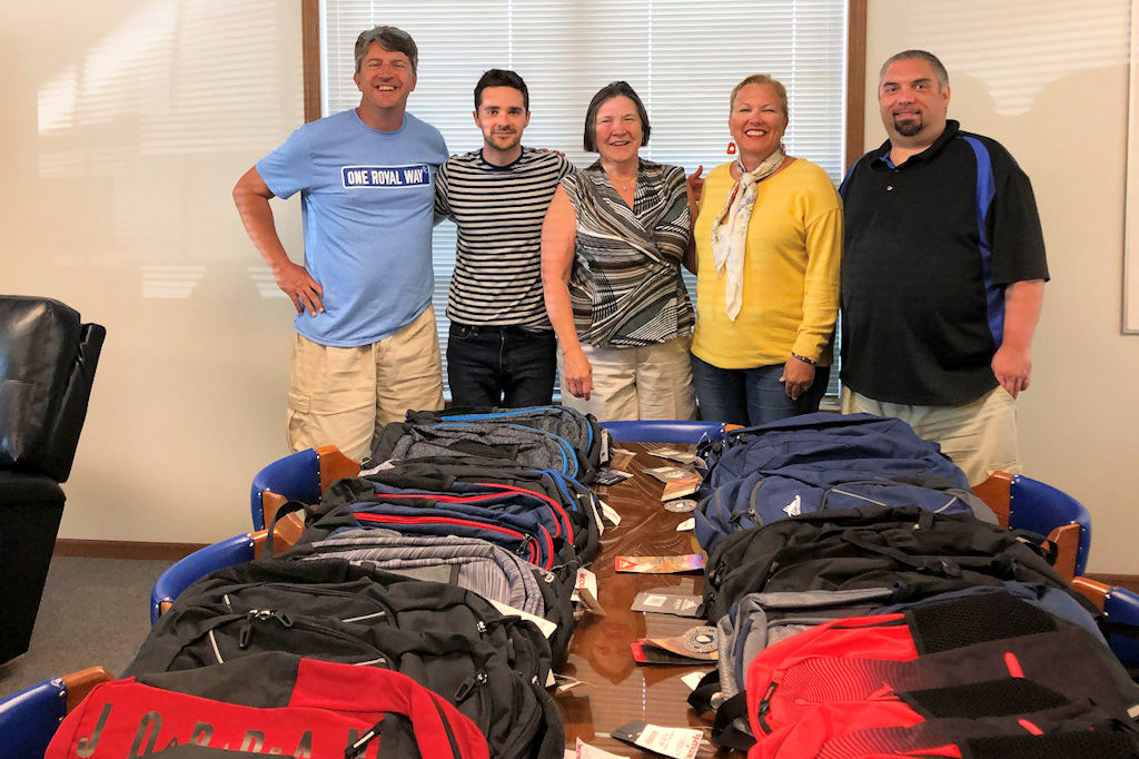 5 people standing beside a table filled with donated backpacks