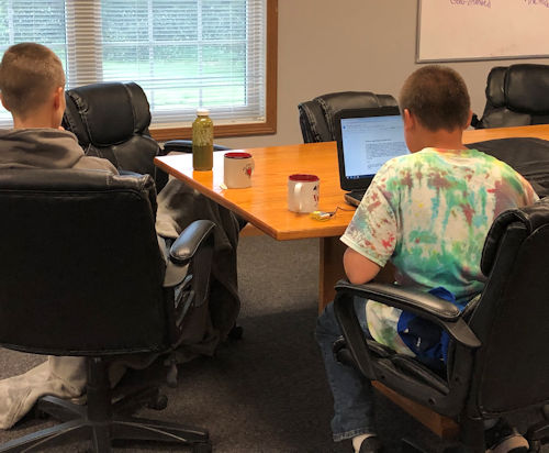 young boys sitting at a table using a laptop