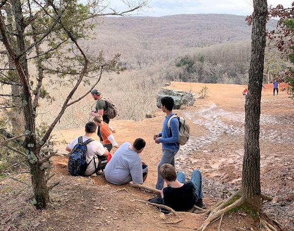 Young men sitting on a dirt path with trees surrounding them