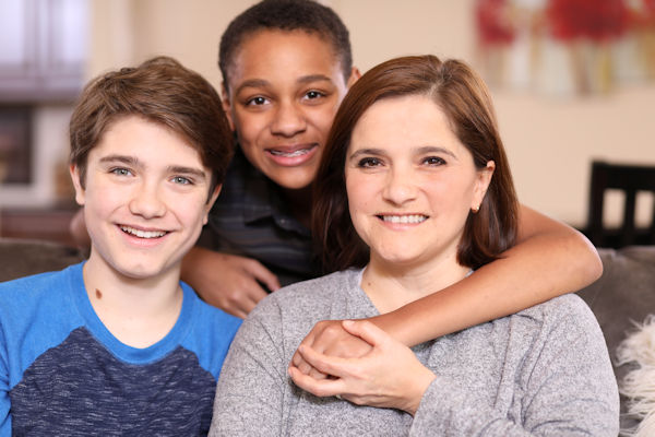 Multi-ethnic family members at home sharing a hug. Single latin descent mother at right. Adopted child center.