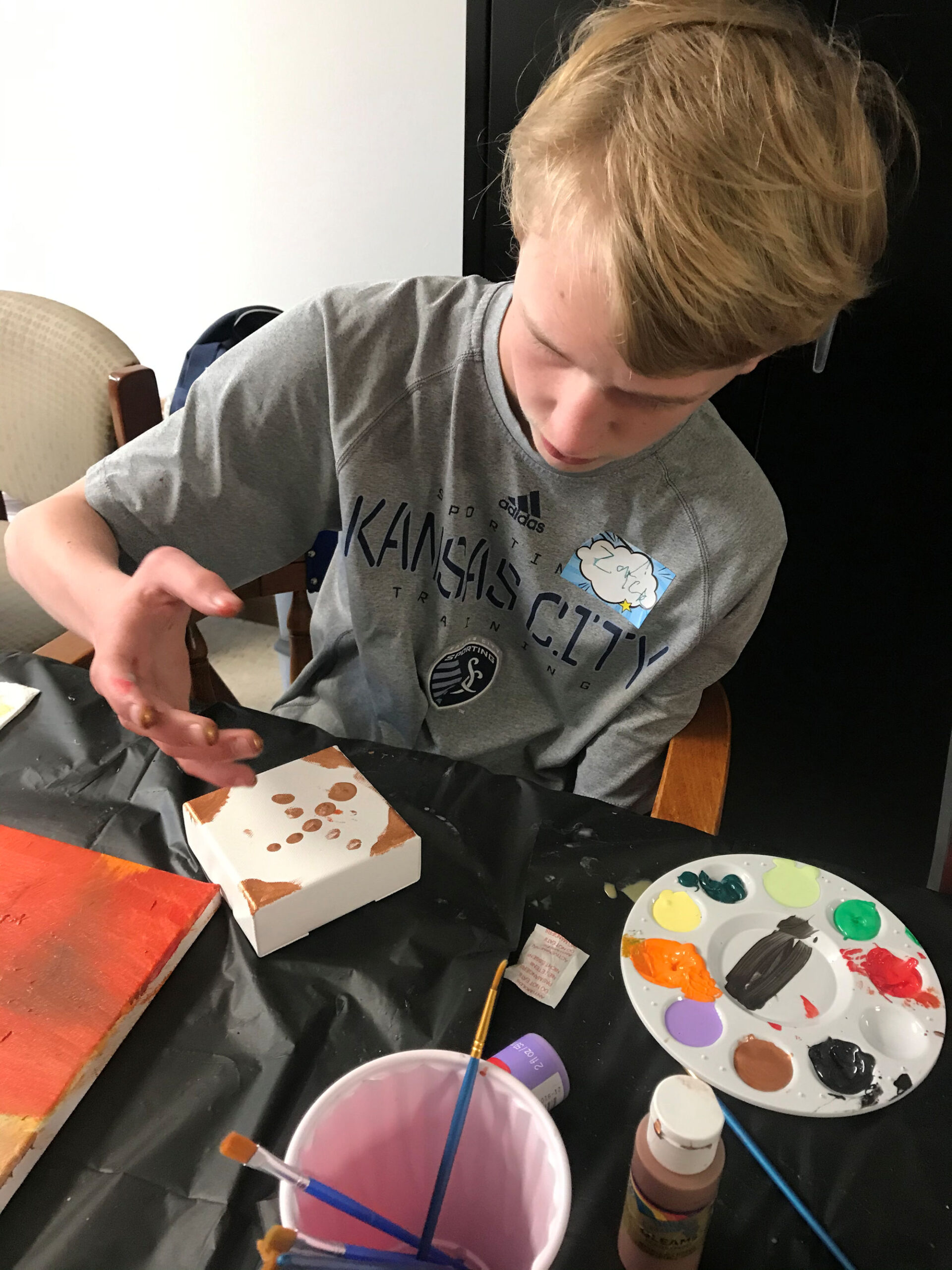 young man sitting at a table with paint and paint brushes doing artwork